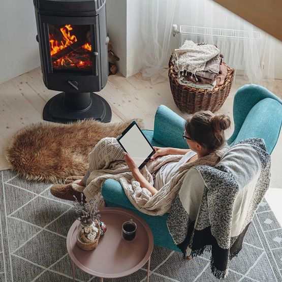 frau sitzt in einem gemütlichen sessel mit warmer decke und benutzt ein tablet